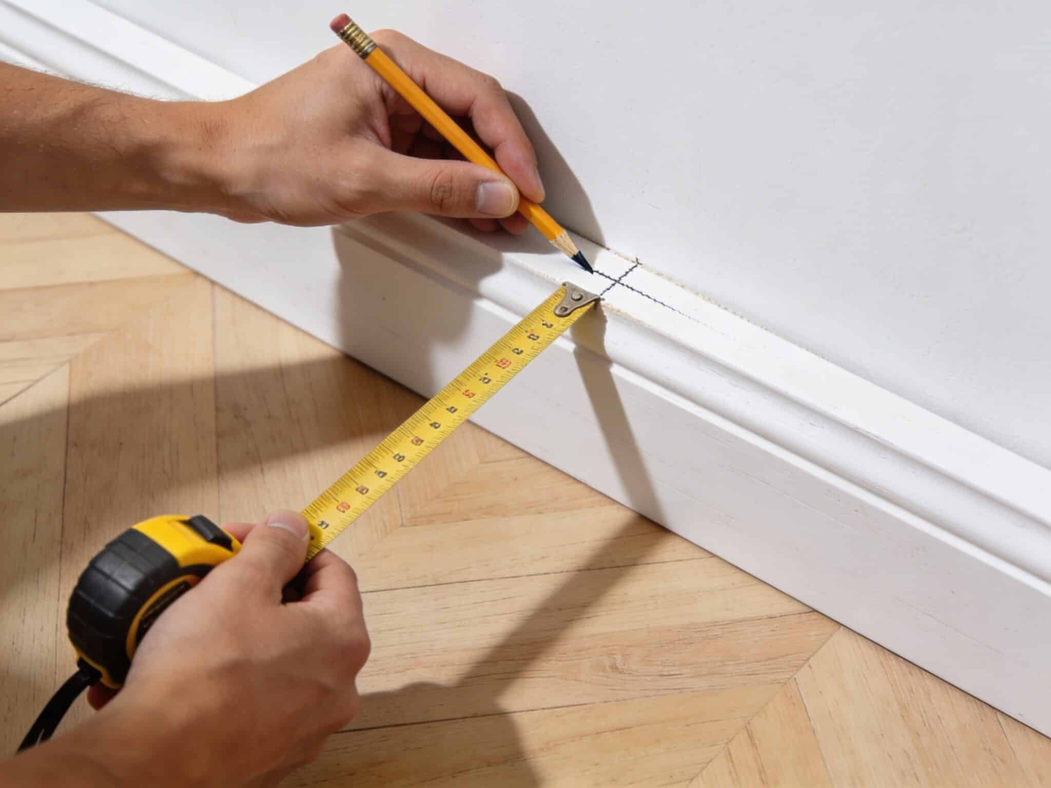 Mesure et marquage d'une plinthe au mètre ruban et au crayon avant la coupe à 45 degrés